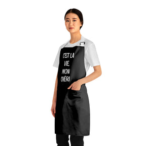 side view of a woman wearing a black grilling apron with white straps with says "c'est la vie, mon chéri"