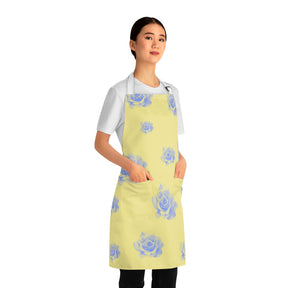 side view of girl wearing a grilling apron with a yellow and blue rose pattern on it and white straps with both hands in apron pockets