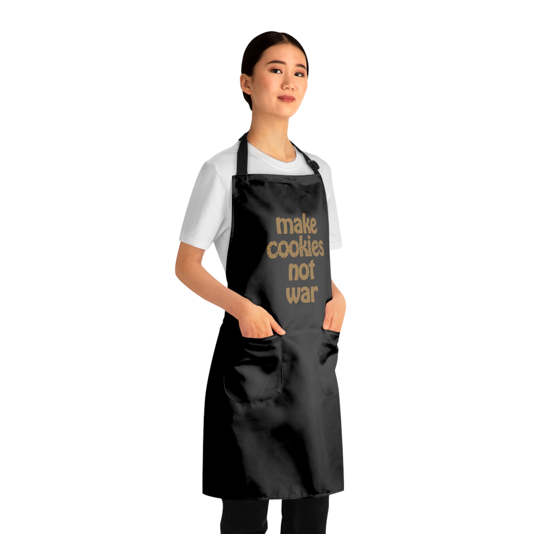 side view of a girl wearing a black apron that says "make cookies not war" with both hands in the front pockets