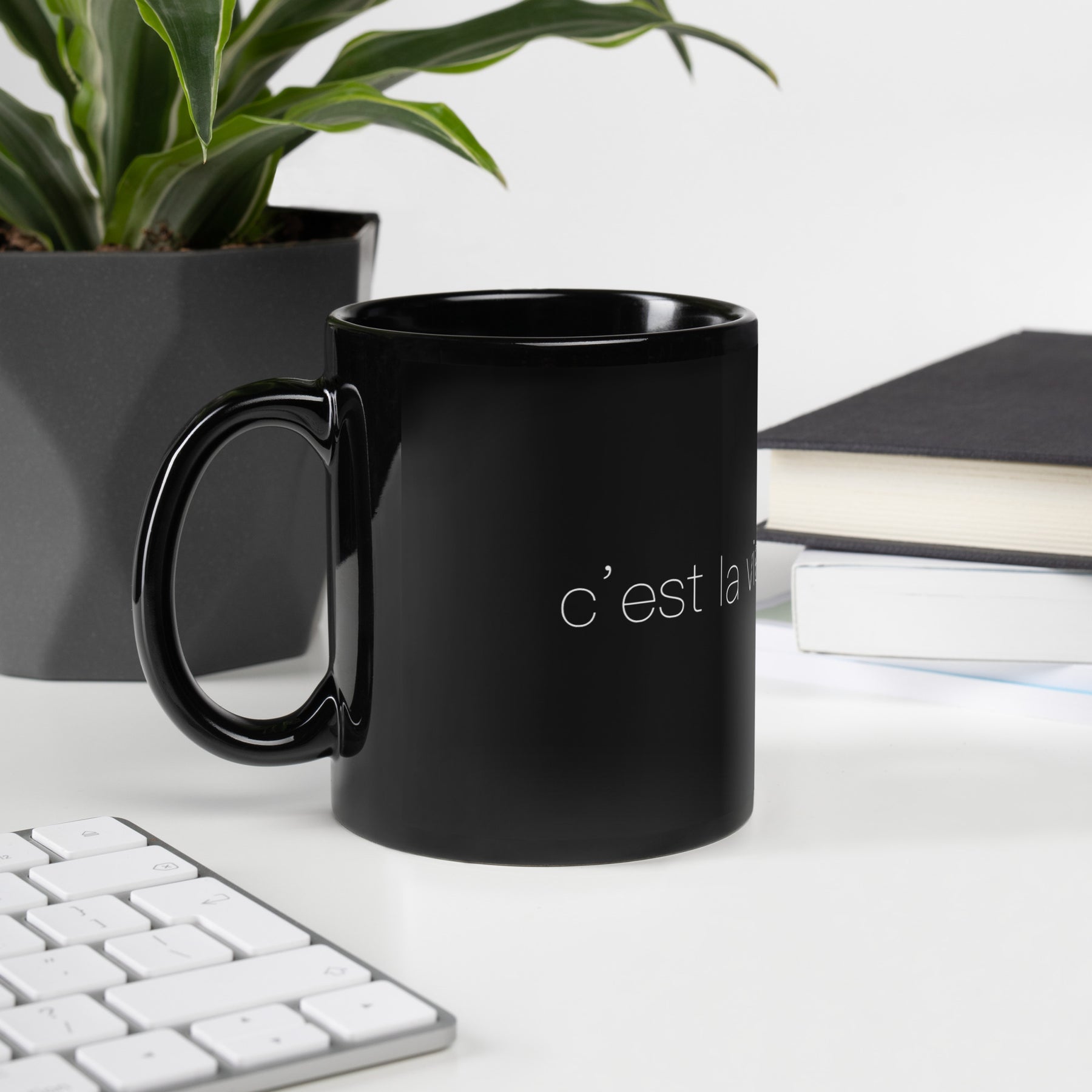 Side view of a black mug on a desk that says "c'est la vie, mon chéri"