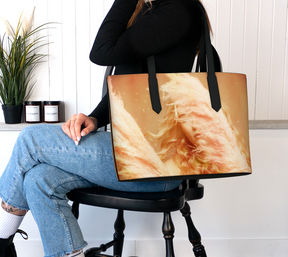 seated woman holding a vegan leather tote bag of a photograph of a young blonde girl holding pink fluffy plumes